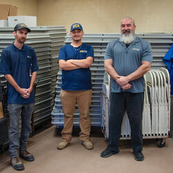 People standing in front of stacked tables, chairs, and dolly equipment