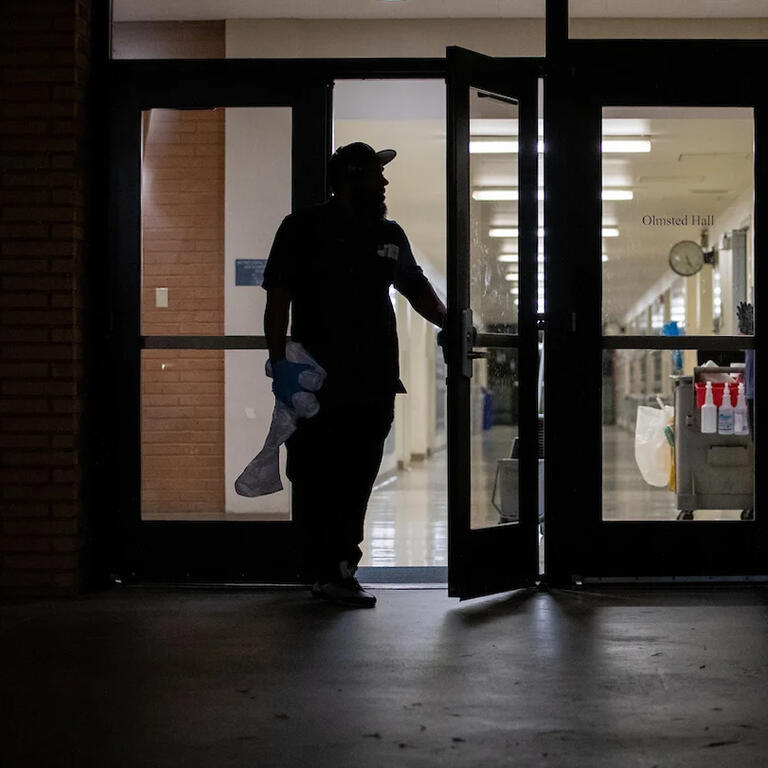 Custodial leaving building with supplies at night