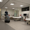 A custodian riding cleaning equipment past medical beds