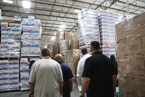 People looking at packaged paper products stacked in a warehouse