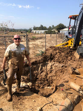 Excavation work at an agricultural site, with a worker standing beside a deep trench