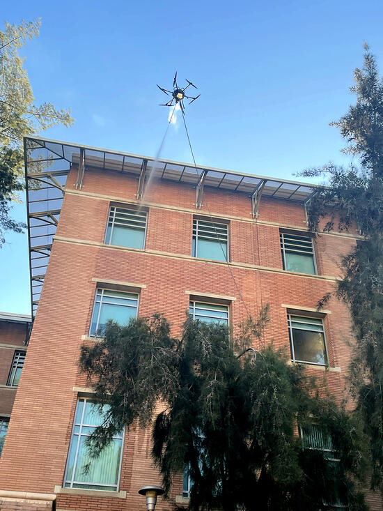 A drone power washes a window of a high-rise brick building